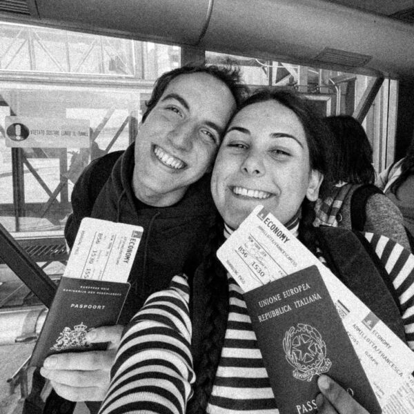 due ragazzi sorridenti in aeroporto con dei passaporti in mano